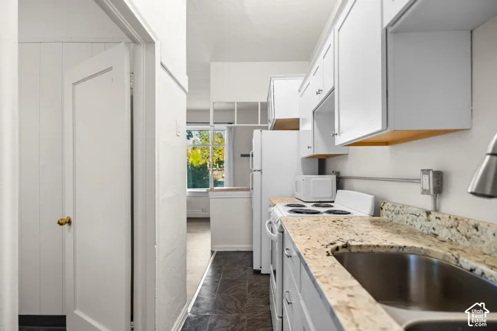 Kitchen featuring white cabinetry, light-toned speckled countertops, a stainless steel sink, and white appliances