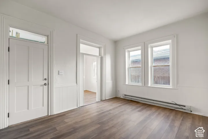 Wood-finish flooring, white paneled door with transom window, white wainscoting, and double windows with white trim