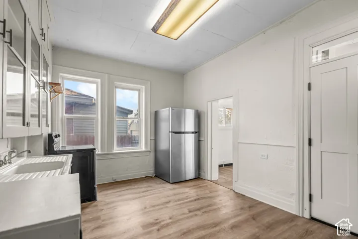 Wood-finish flooring, white cabinetry with glass panels, dual windows, stainless steel refrigerator, and a built-in sink