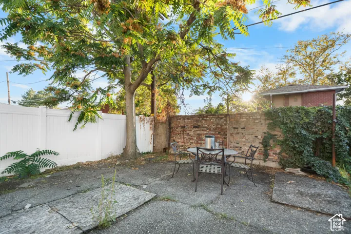 Paved patio space featuring a prominent mature tree, white privacy fencing, and a brick wall