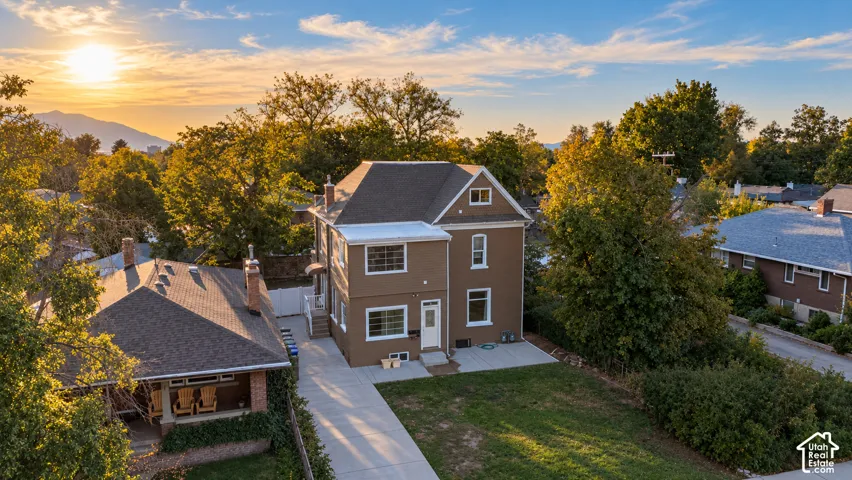 Brown stucco exterior, asphalt shingle roof, concrete driveway, mature trees, mountain backdrop