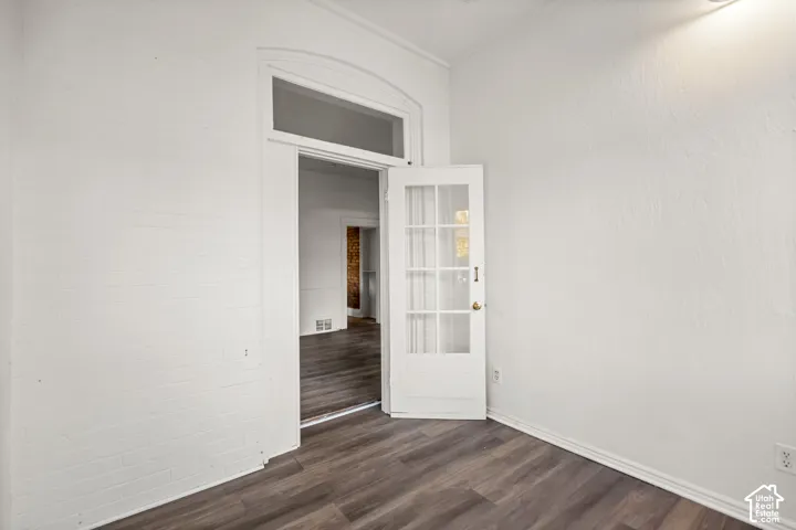 Wood-finish flooring, white painted brick accent wall, and a french door with arched transom