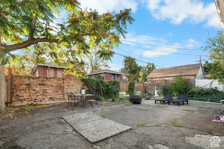 Expansive outdoor space featuring a brick privacy wall, a substantial mature tree, and a detached structure with a pitched roof