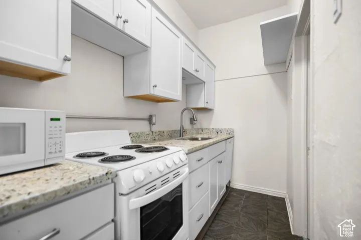 White shaker-style cabinetry, light-toned countertops, stainless steel sink with a gooseneck faucet, and dark-toned floor tiles