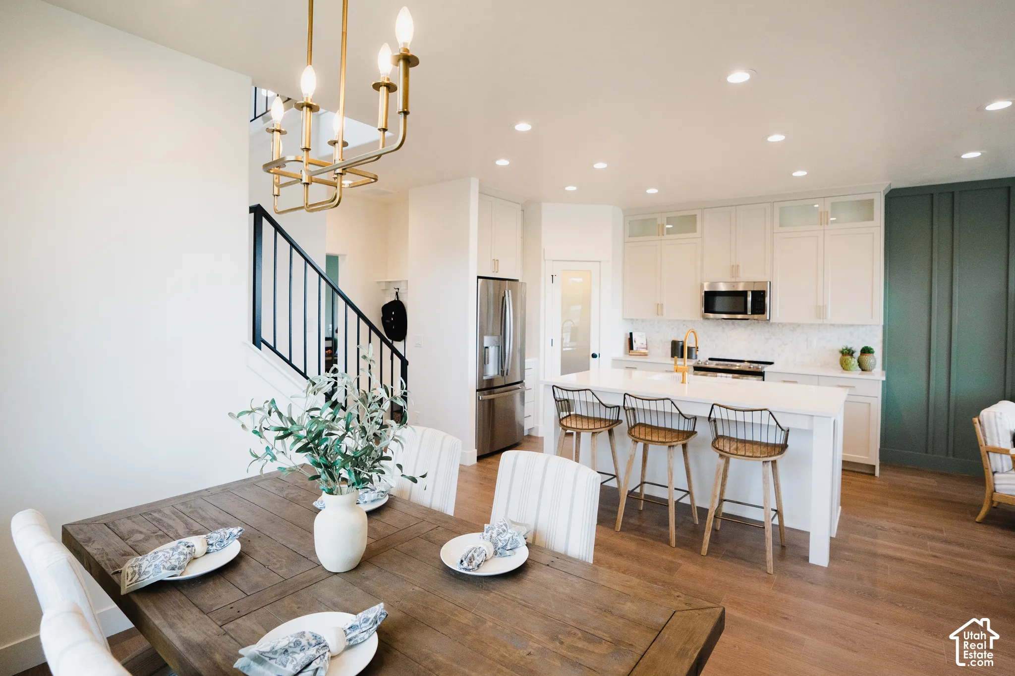 Open-concept kitchen and dining area featuring a white kitchen island, stainless steel appliances, wood-finish flooring, and white cabinetry with glass-front uppers
