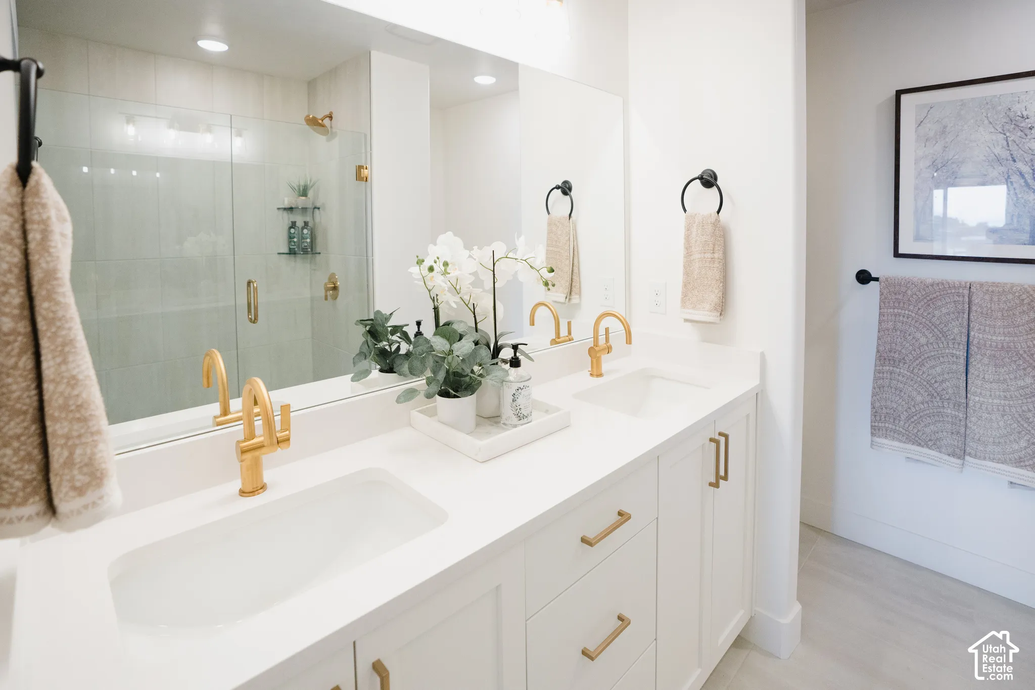 Dual vanity with integrated sinks, white countertops, gold-tone fixtures, white cabinetry, and large mirrored wall