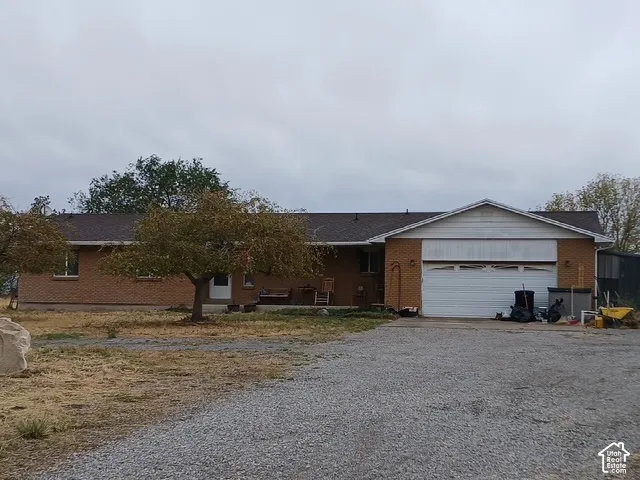 Brick exterior residence with a gravel driveway, attached garage, and mature trees