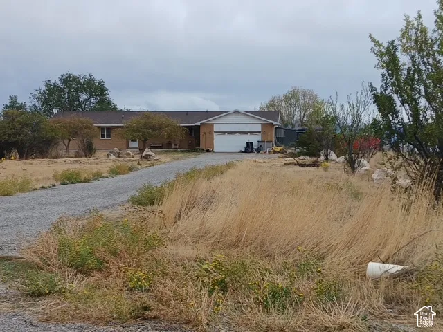 Gravel driveway leading to a residence with a light brown brick facade, white trim, and an attached garage
