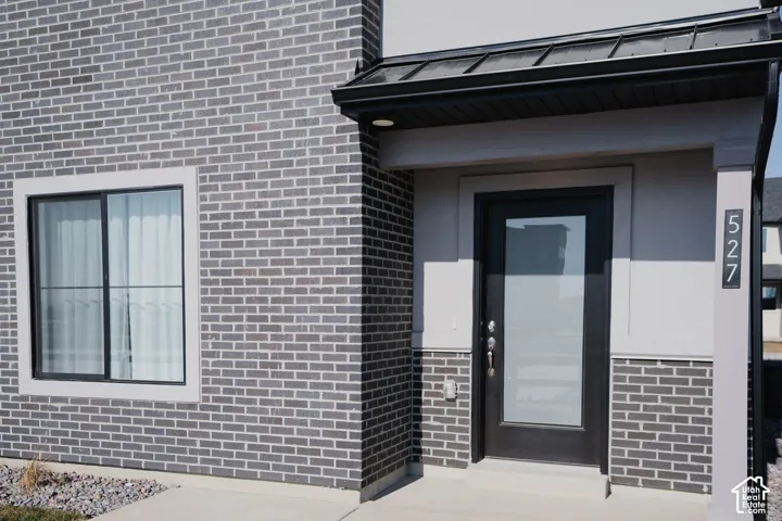 Modern exterior featuring gray brick, a covered entry, a black framed window, a black entry door with frosted glass, and metal roof accents