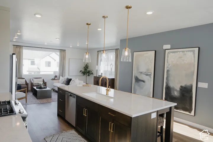 Open-concept kitchen and living area featuring a large center island with a sink, stainless steel dishwasher, and brass hardware