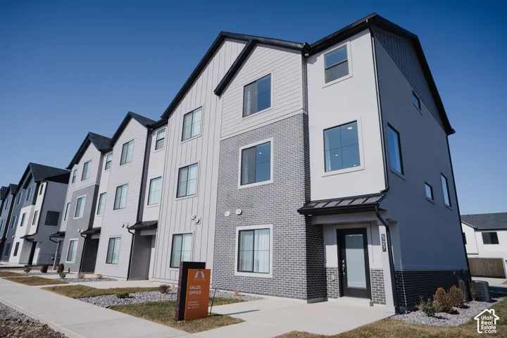 Modern three-story townhouse featuring a multi-textured facade with vertical siding, stucco, and brick accents