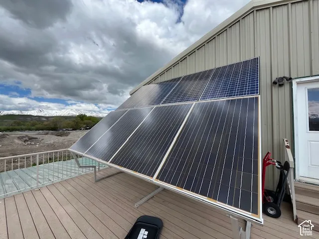 Deck with visible solar panel installation, a metal exterior wall, and snow-capped mountains in the background