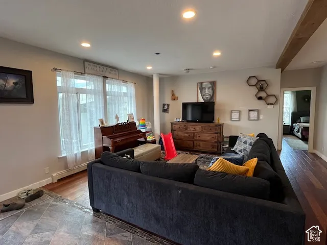 Recessed ceiling lighting, large windows, wood-finish flooring, exposed ceiling beam, and a wide entryway