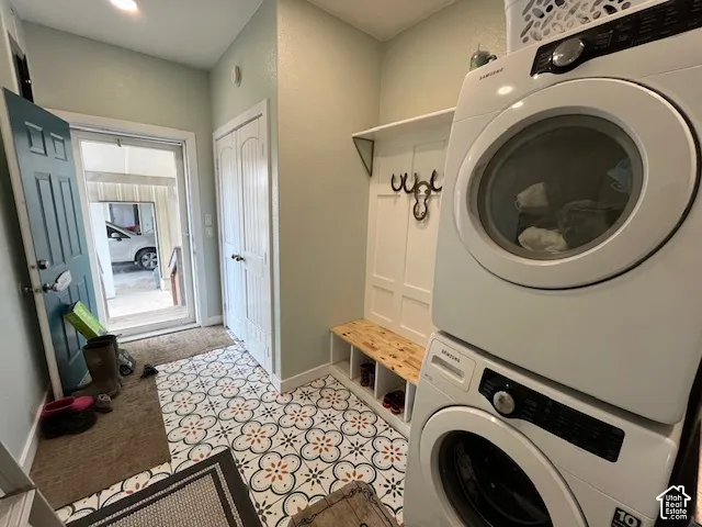 Patterned floor tiling, built-in mudroom bench with storage, stacked laundry appliances, and a built-in coat rack