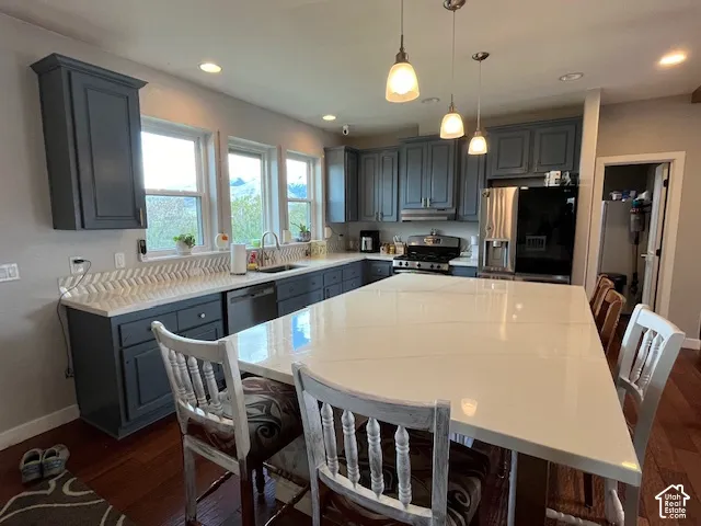 Kitchen featuring an expansive island with a white countertop, dark shaker-style cabinetry, stainless steel appliances, a chevron-patterned backsplash, and wood-finish flooring