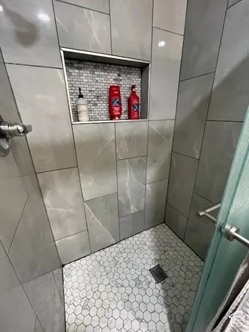Shower enclosure featuring large format wall tiles, a built-in recessed niche with mosaic tile, and a hexagonal floor tile