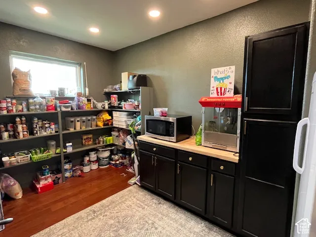 Recessed ceiling lighting, a window, wood-finish flooring, and dark cabinetry with light-toned countertops