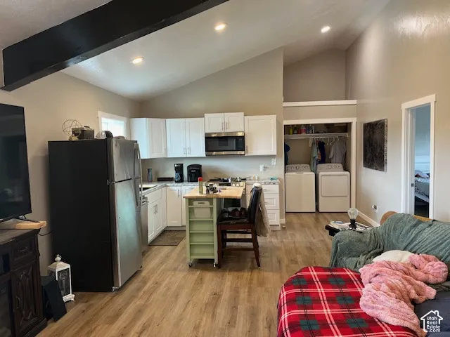 Vaulted ceilings, wood-finish flooring, white cabinetry, stainless steel appliances, and an in-unit laundry area
