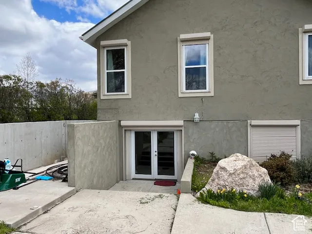 Stucco exterior with multiple windows, concrete retaining wall, and double glass door entry
