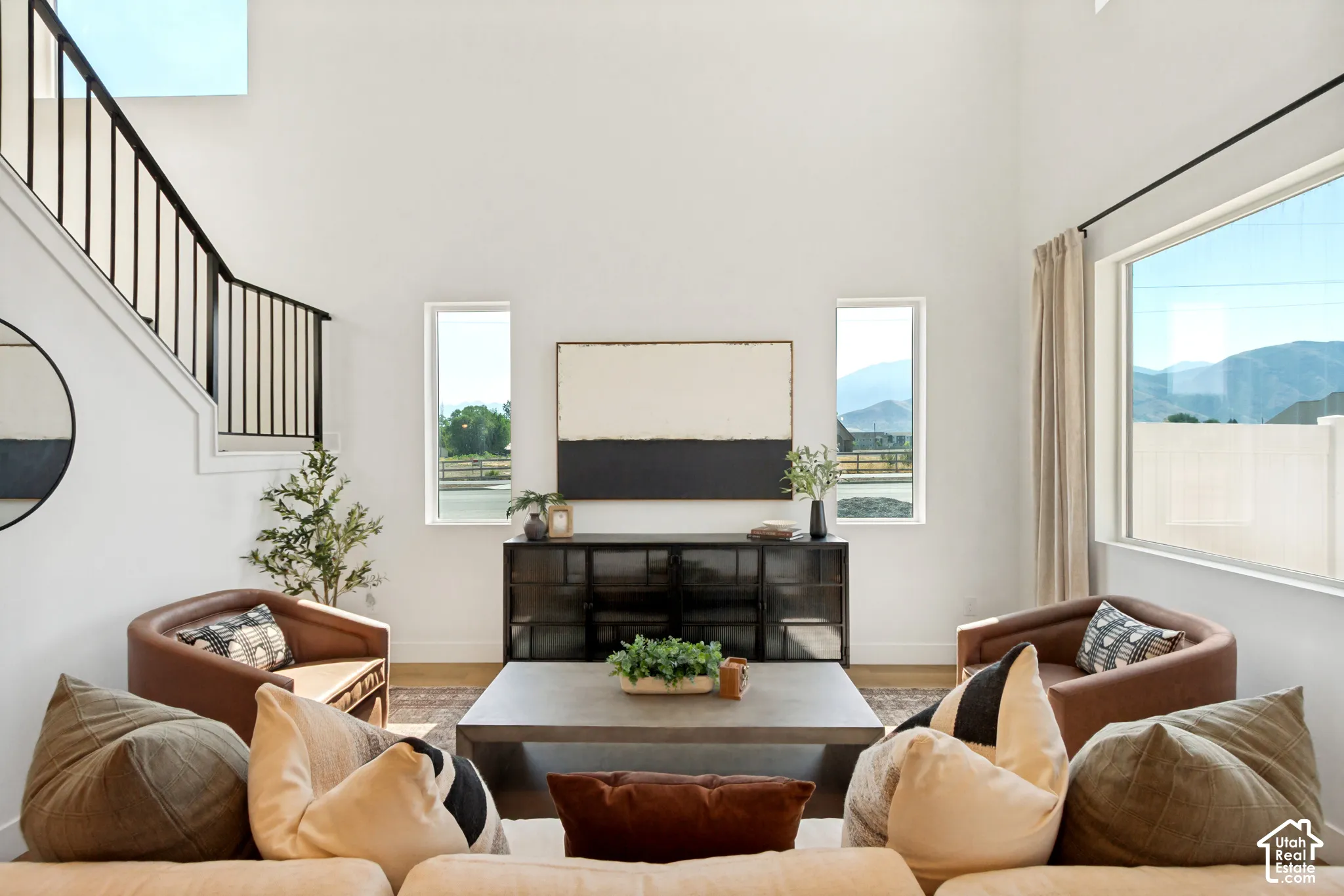 Vaulted ceiling, large picture windows, wood-finish flooring, staircase with metal railing, white walls