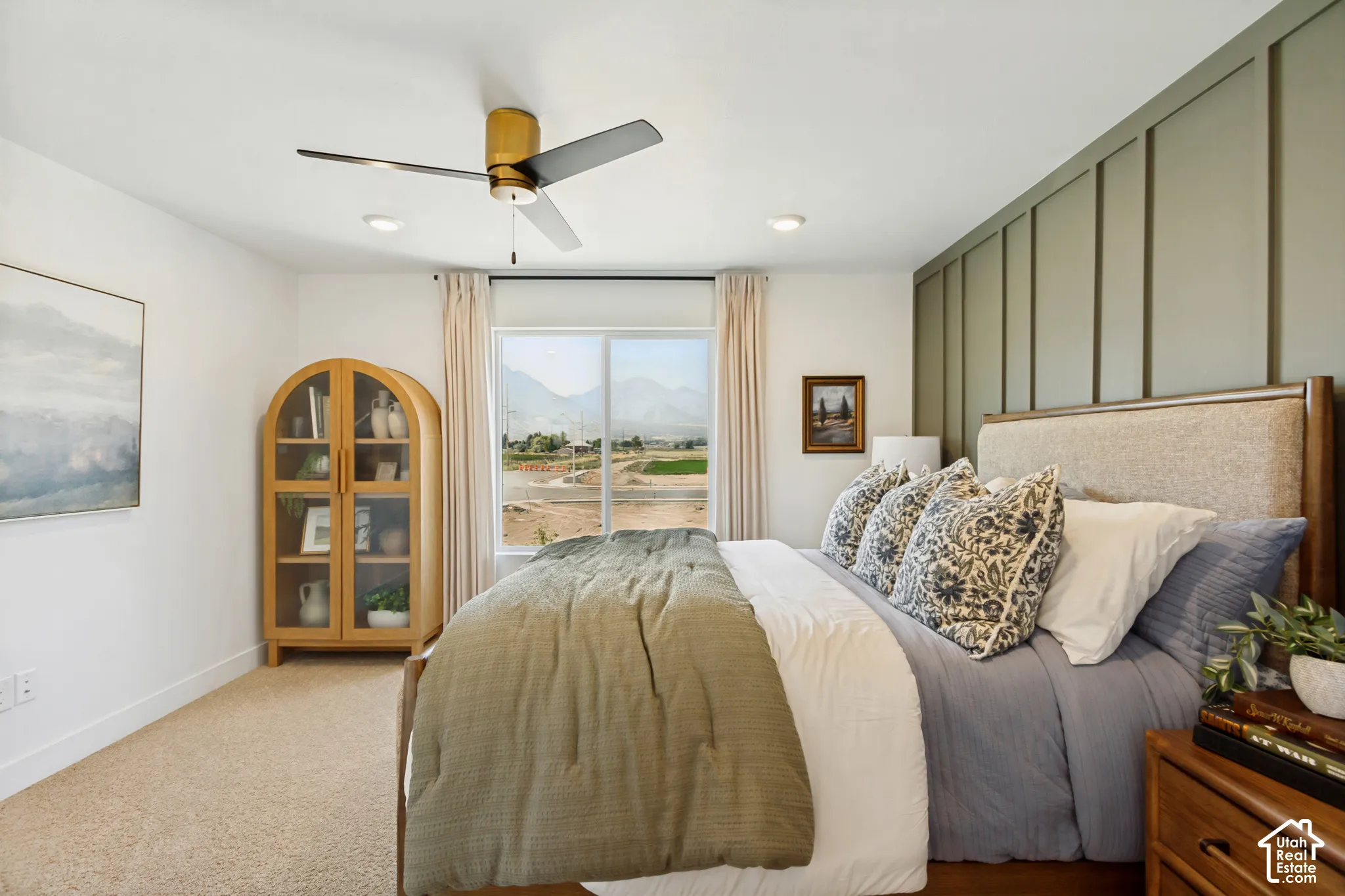 Recessed ceiling lighting, a contemporary ceiling fan with a gold-tone motor, a prominent window with mountain scenery, and a paneled accent wall