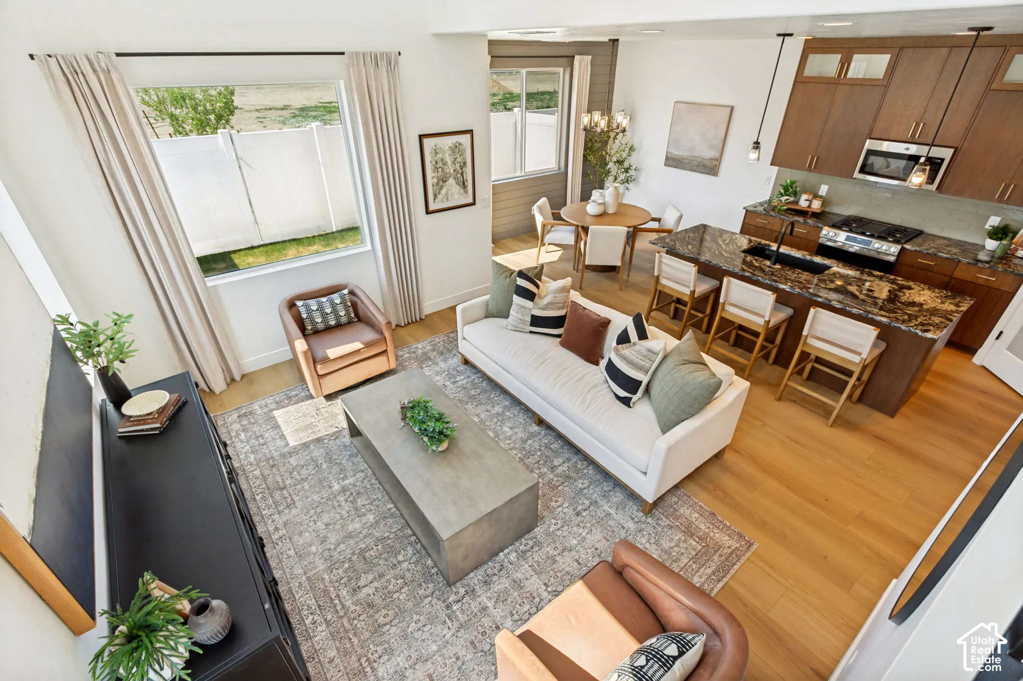 Open-concept living area featuring light wood-finish flooring, a kitchen island with seating, a built-in oven, and pendant lighting fixtures