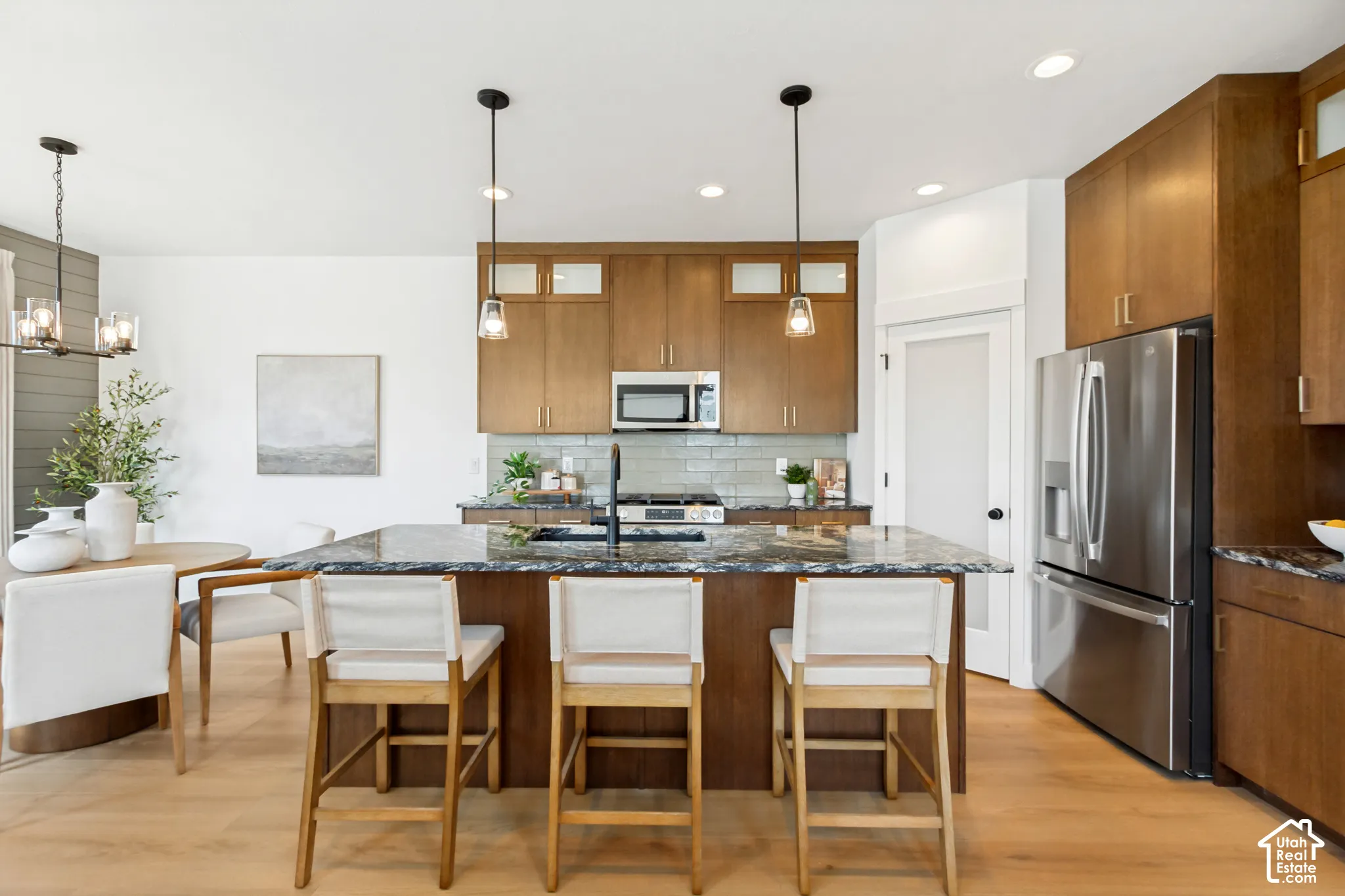 Kitchen featuring a large island with stone countertop, stainless steel appliances, wood-finish cabinetry, a tile backsplash, and wood-finish flooring