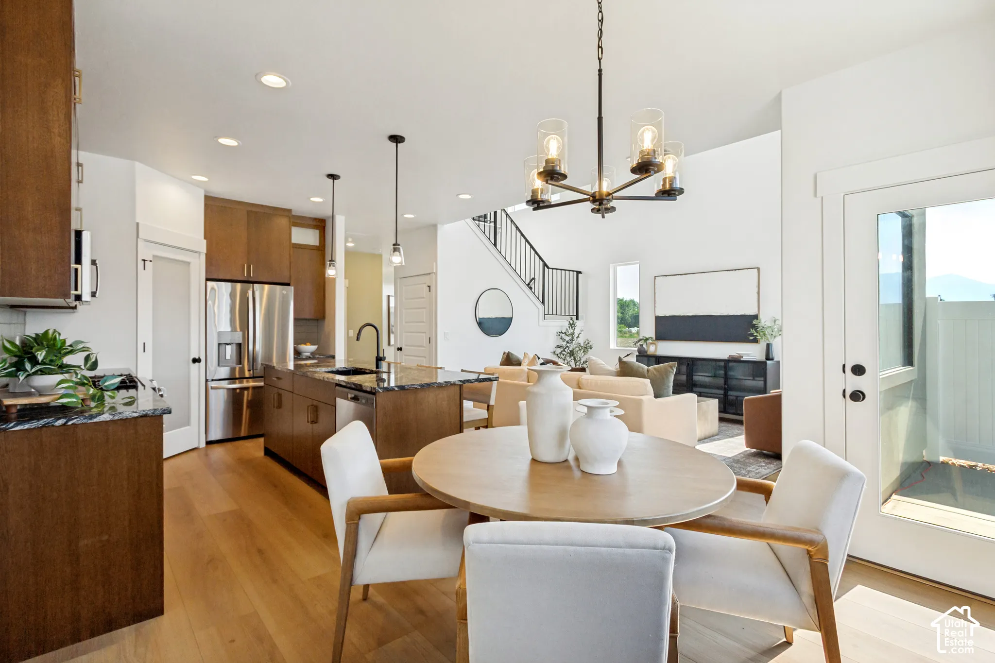 Open-concept living space with wood-finish flooring, a contemporary chandelier, stainless steel refrigerator, and a kitchen island with a dark countertop