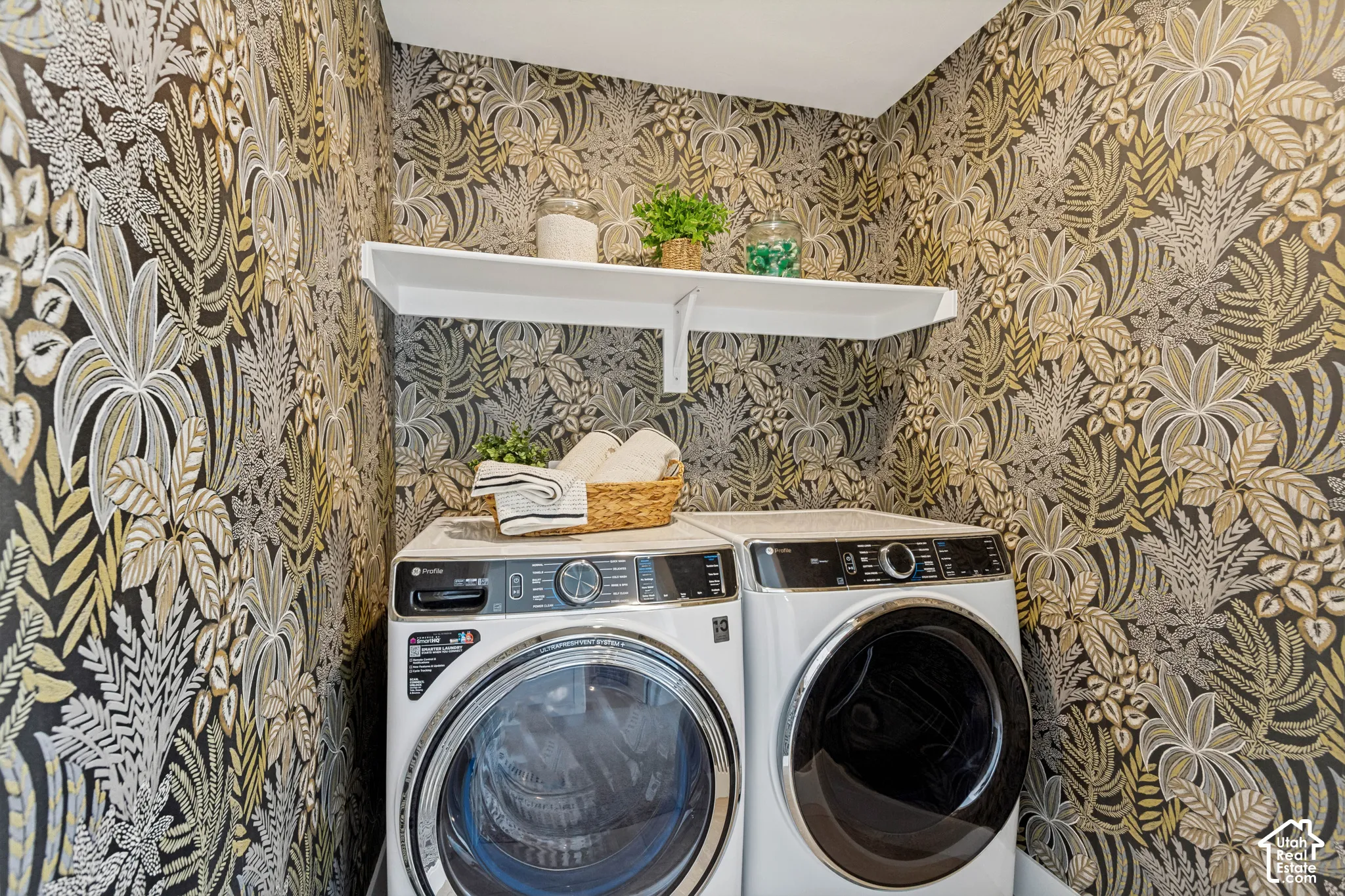 Laundry area featuring patterned wallpaper, white wall-mounted shelving, and appliances
