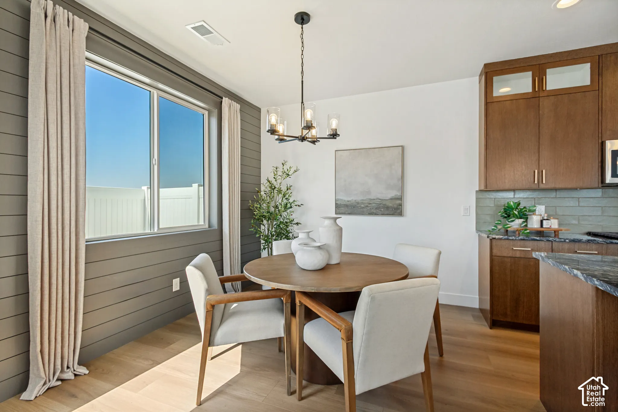 Wood-finish flooring, accent shiplap wall, contemporary chandelier, wood cabinetry, and a tile backsplash
