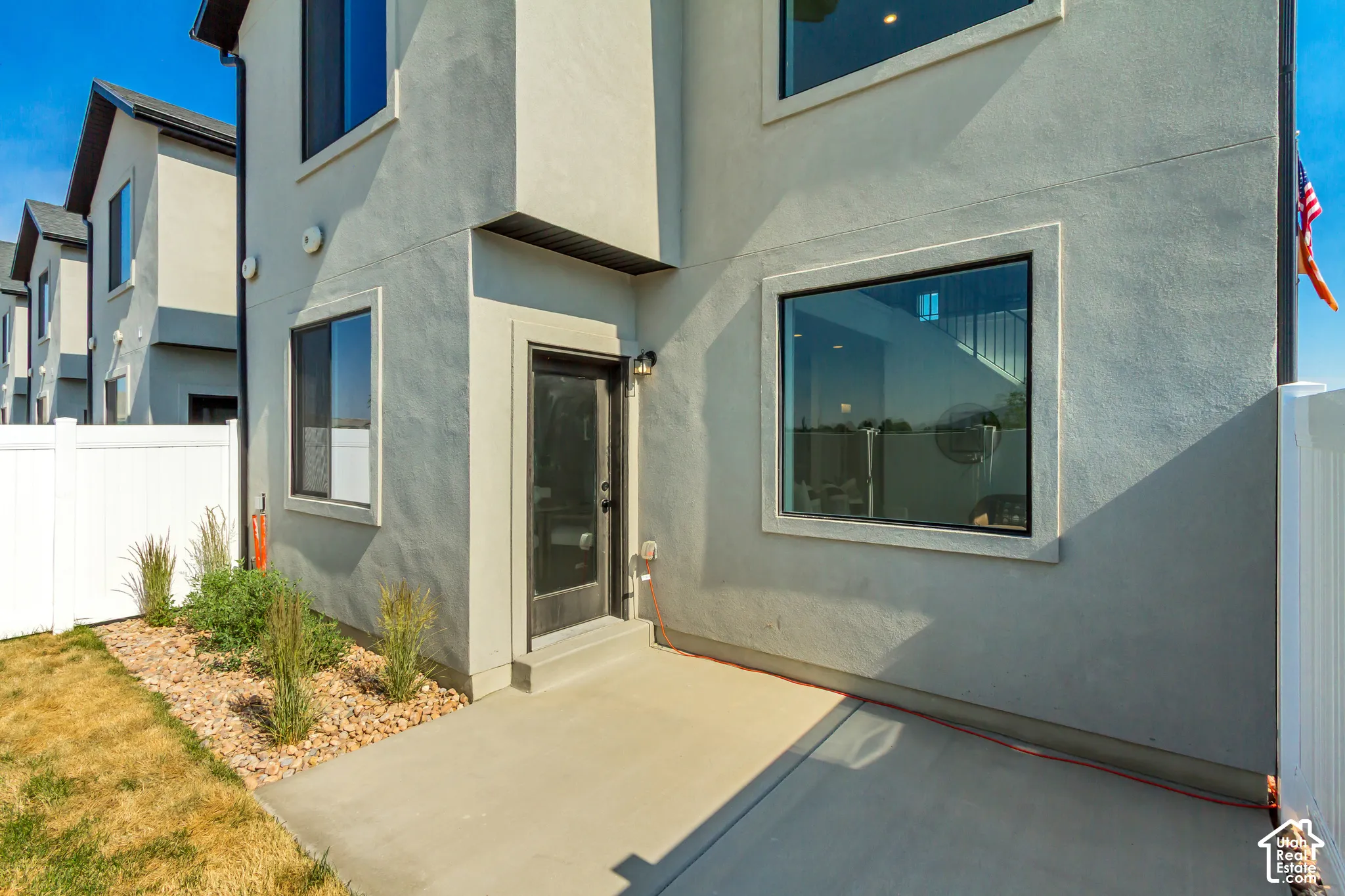 Exterior stucco finish, prominent windows, private patio, gravel landscaping, and white fencing