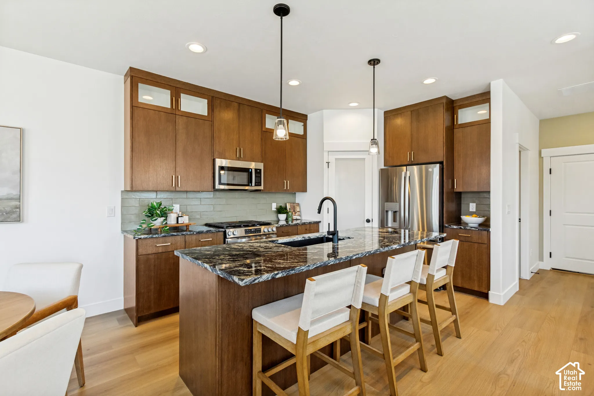 Spacious kitchen featuring wood-finish cabinetry, stainless steel appliances, a dark stone island with seating, and a subway tile backsplash