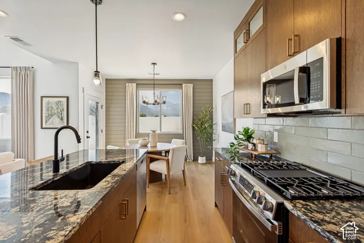 Kitchen featuring wood-finish cabinetry, granite countertops, stainless steel appliances, a tiled backsplash, and wood-finish flooring
