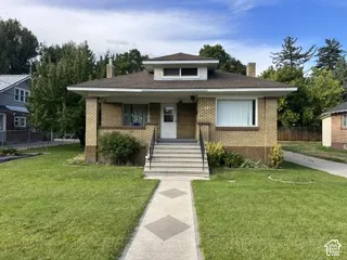 Brick facade with a dormer window, covered front porch, concrete steps, and a patterned walkway