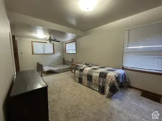 Carpeted room with a ceiling-mounted light fixture, ceiling fan, and two windows with blinds