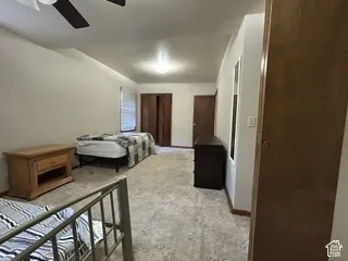 Carpeted flooring throughout, white painted walls, and a ceiling fan with integrated lighting