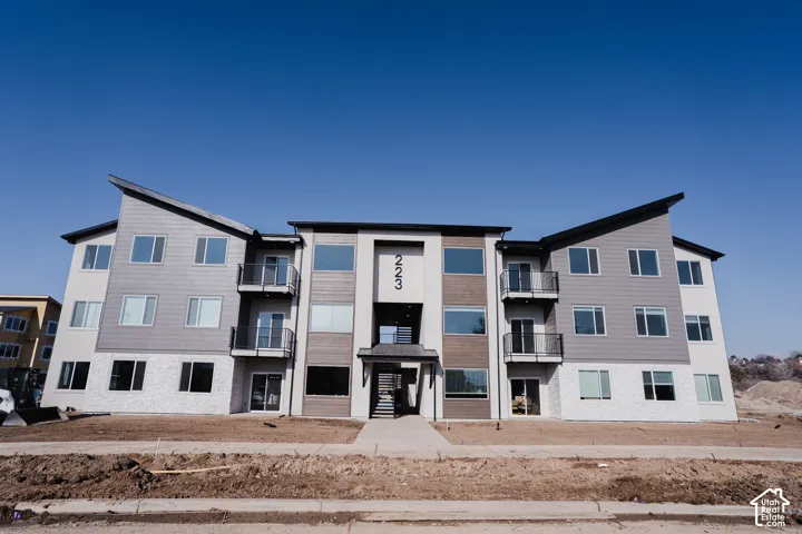 Contemporary multi-story building featuring balconies with black railings, a stone facade, and horizontal siding