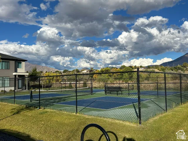 Fenced multi-sport court with a bench, surrounded by green landscaping and a distant mountain backdrop