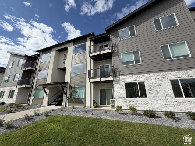 Building exterior featuring horizontal siding, stone veneer, multiple balconies, a covered entrance, and a landscaped frontage