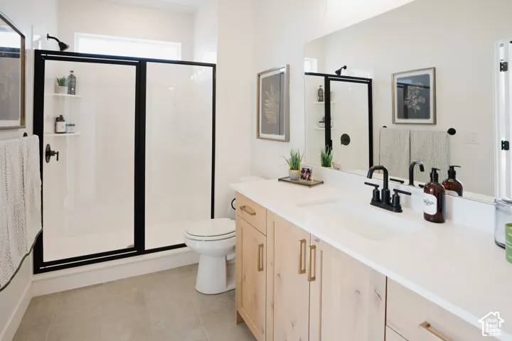 Spacious shower with black-framed glass enclosure, light wood-finish vanity with gold-tone hardware, white countertop with integrated sink, matte black faucet, and large wall-mounted mirror