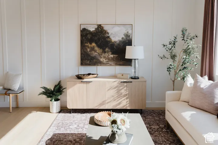 White vertical plank accent wall, wood-finish flooring, built-in cabinetry with metal pulls, and window with solid drapes