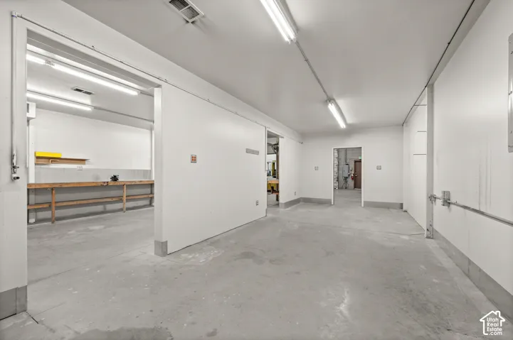 Concrete flooring, recessed lighting, white panel walls, sliding door, and a built-in workbench