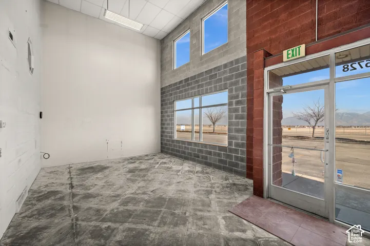 Concrete block construction with red brick accents, expansive window placements, glass entry door with aluminum frame, and exposed concrete flooring
