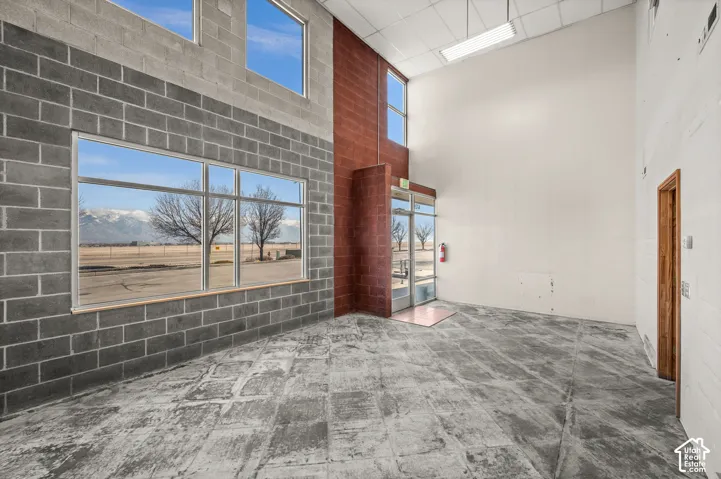 High ceilings with exposed concrete flooring, large window banks, and a glass-paneled entry door