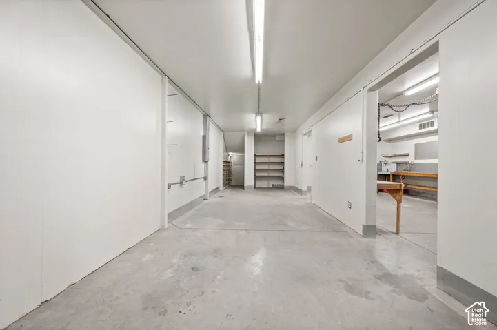 Concrete flooring, white walls, built-in shelving, and exposed overhead lighting