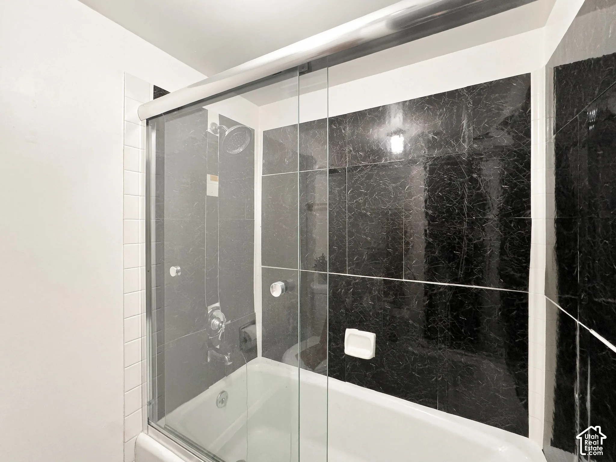 Built-in bathtub with shower, black marbled wall tiling, white subway tile accents, and sliding glass shower door