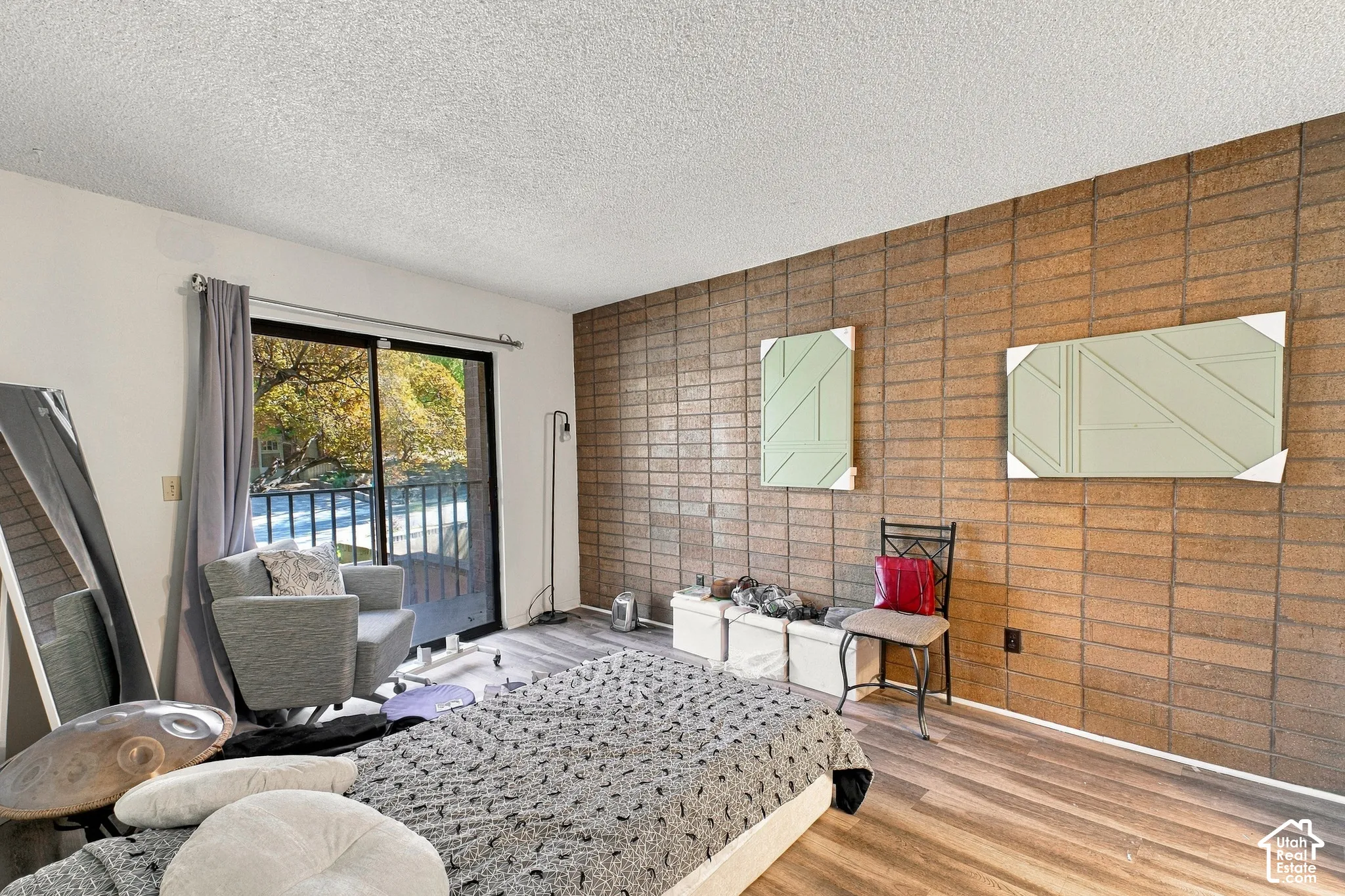 Sliding glass door, wood-finish flooring, textured accent wall, and a balcony with black railings