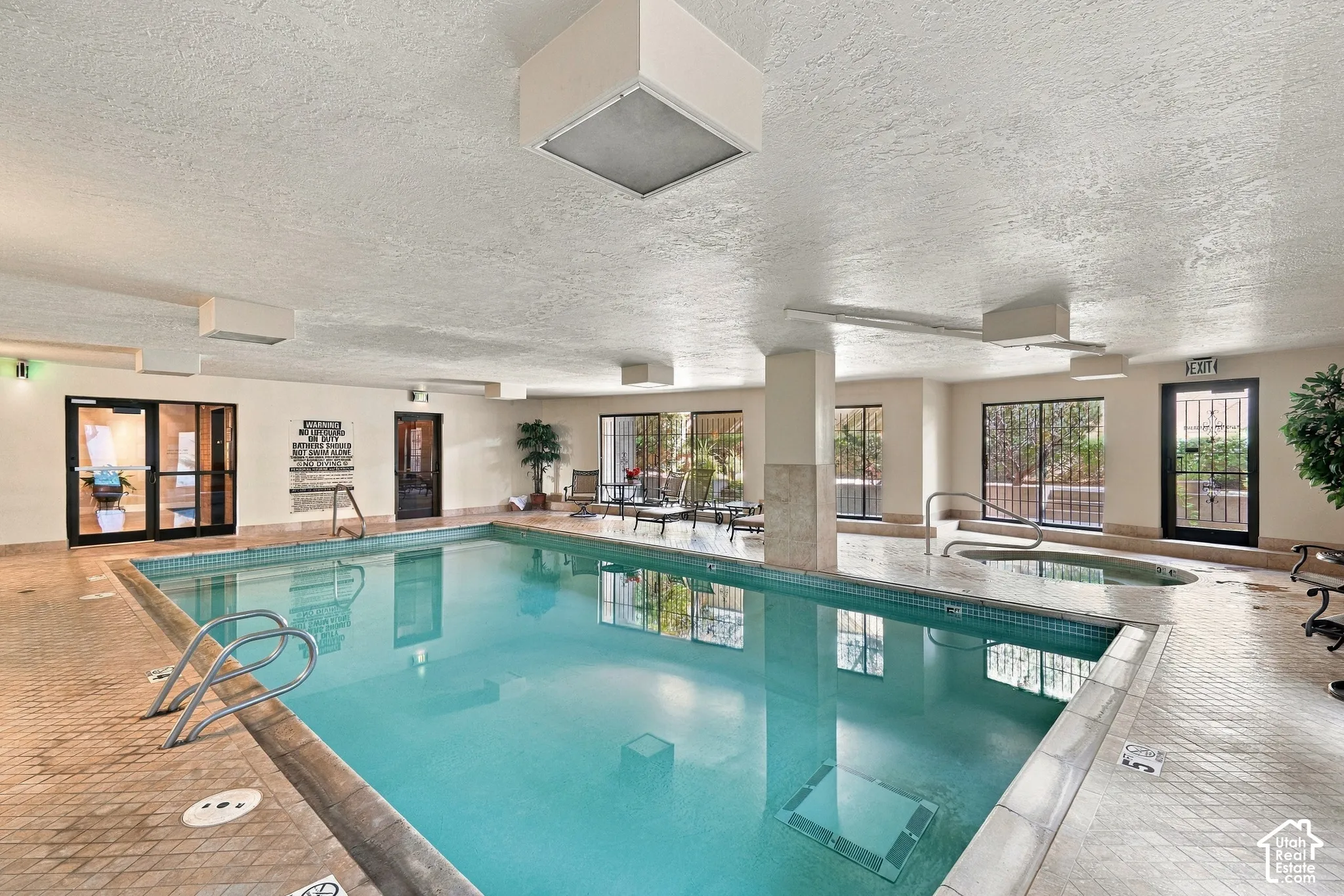 Indoor swimming pool with an integrated hot tub and perimeter tile detailing, surrounded by tiled decking