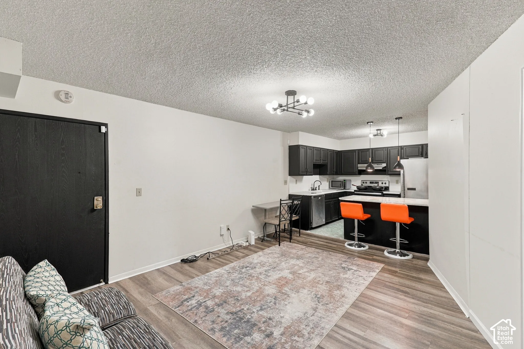 Open-concept living space featuring wood-finish flooring, a modern chandelier, dark cabinetry, and stainless steel appliances