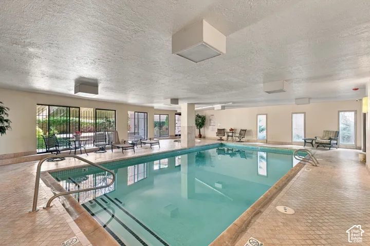 Indoor swimming pool featuring tiled surround, multiple window openings, and recessed overhead lighting